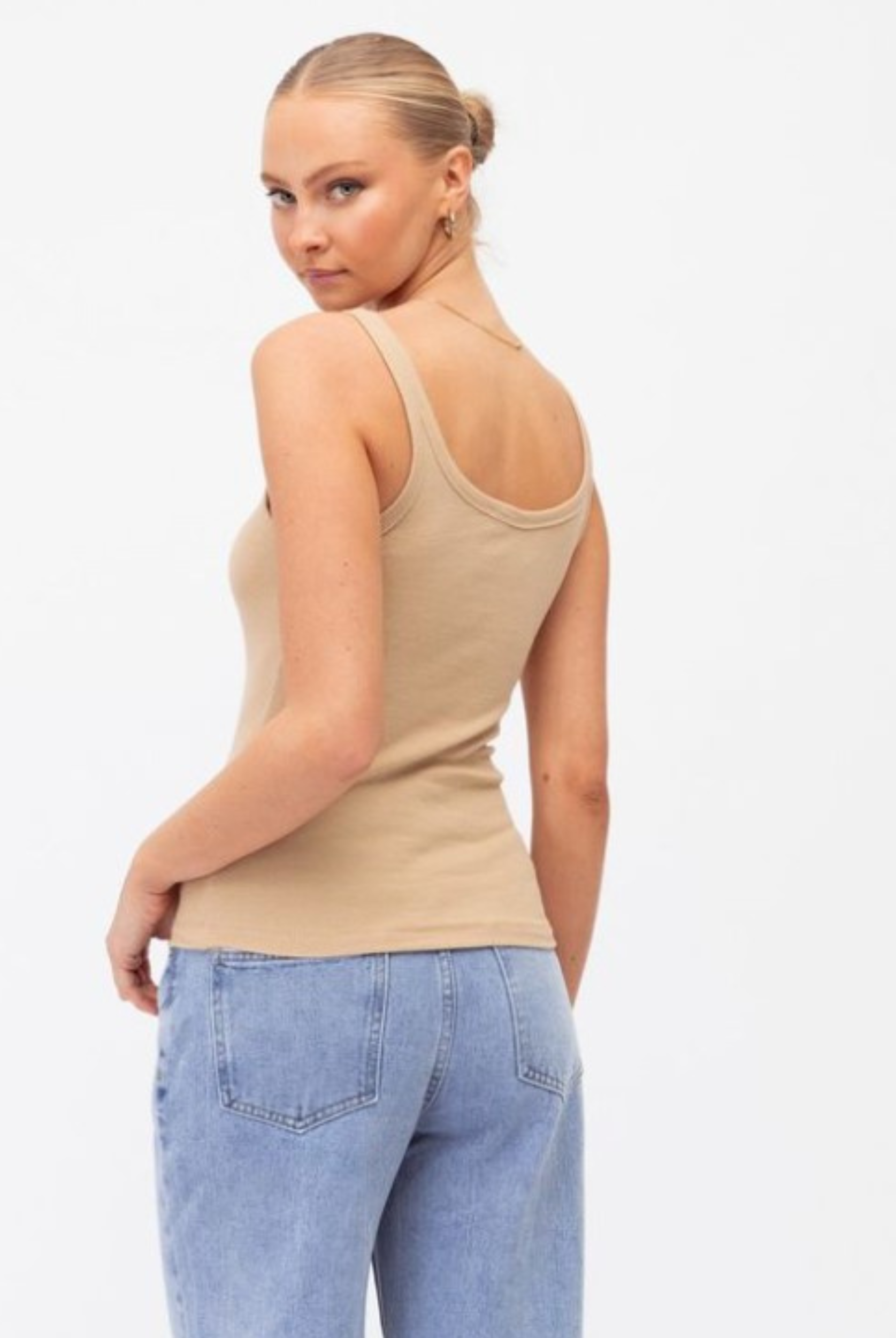 Model wearing a neutral tank with lightwash denim jeans