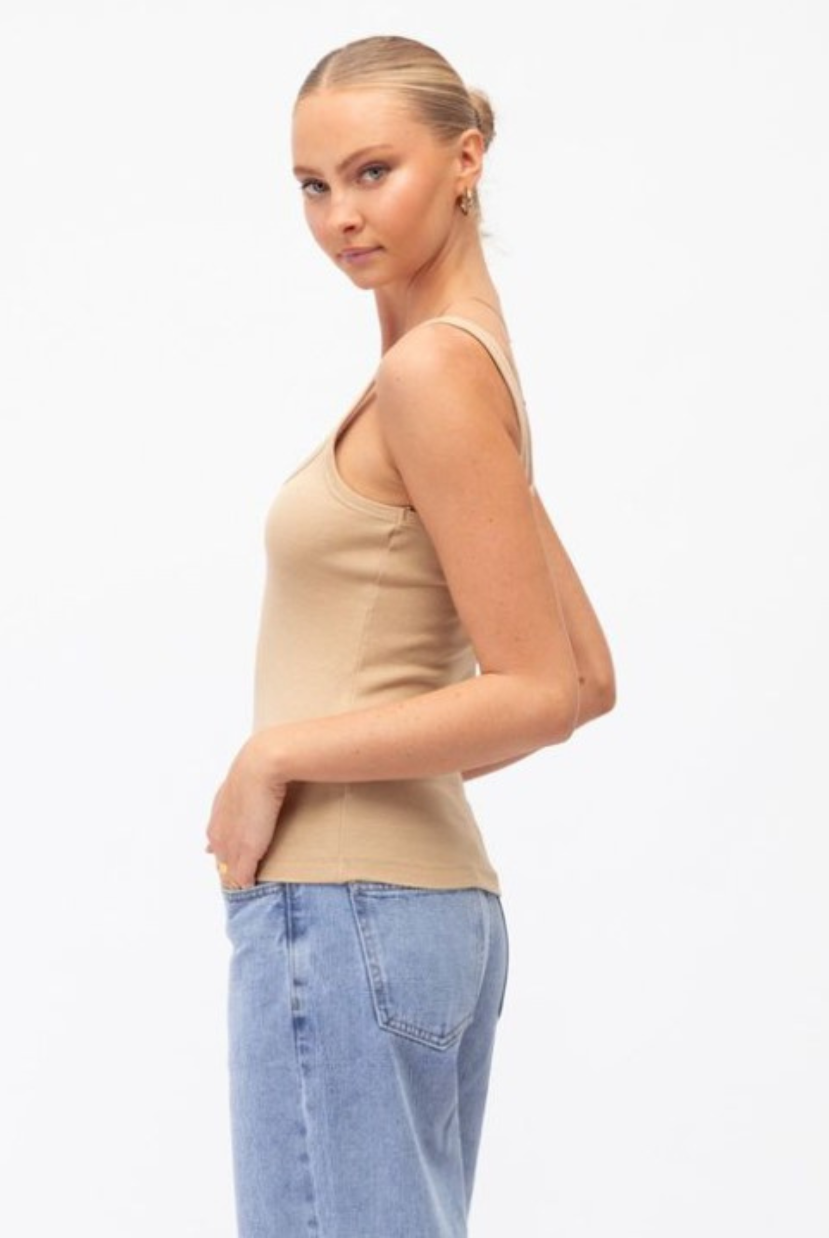 Model wearing a neutral tank with lightwash denim jeans