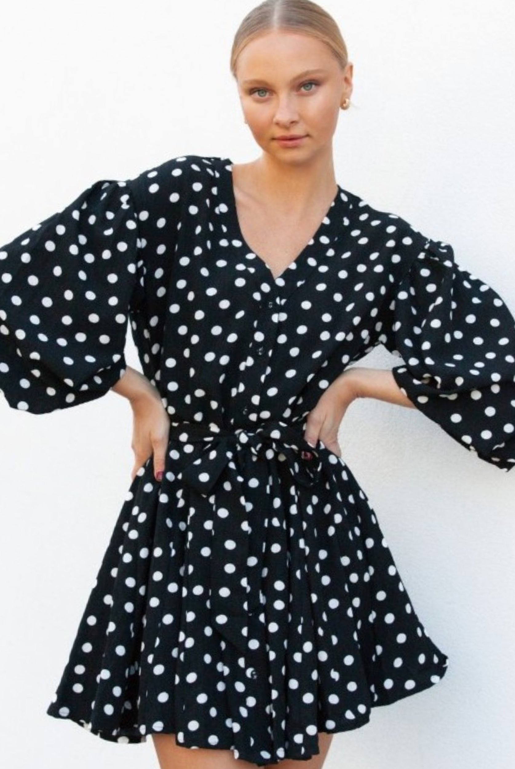 Model wearing black and white polka dot dress with waist belt and buttons