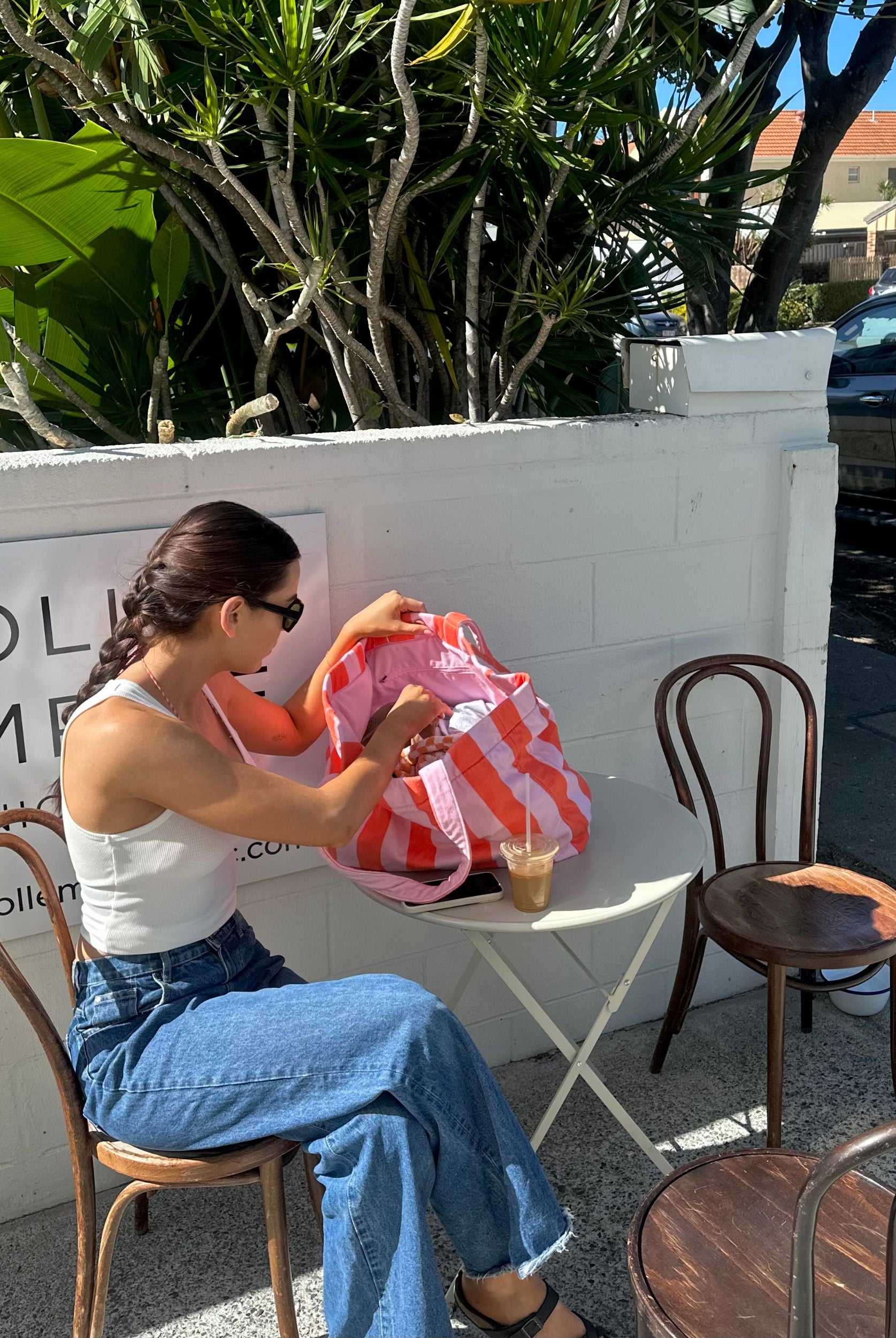 Woman sitting at a table outdoors, opening a pink bag.
