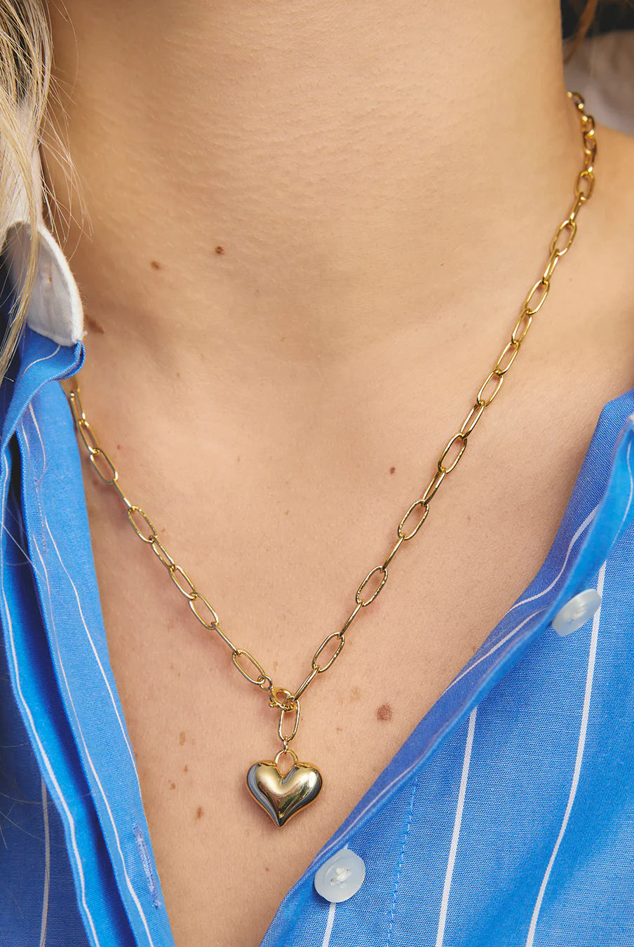 Gold chain necklace with a heart pendant worn by a person in a blue shirt.