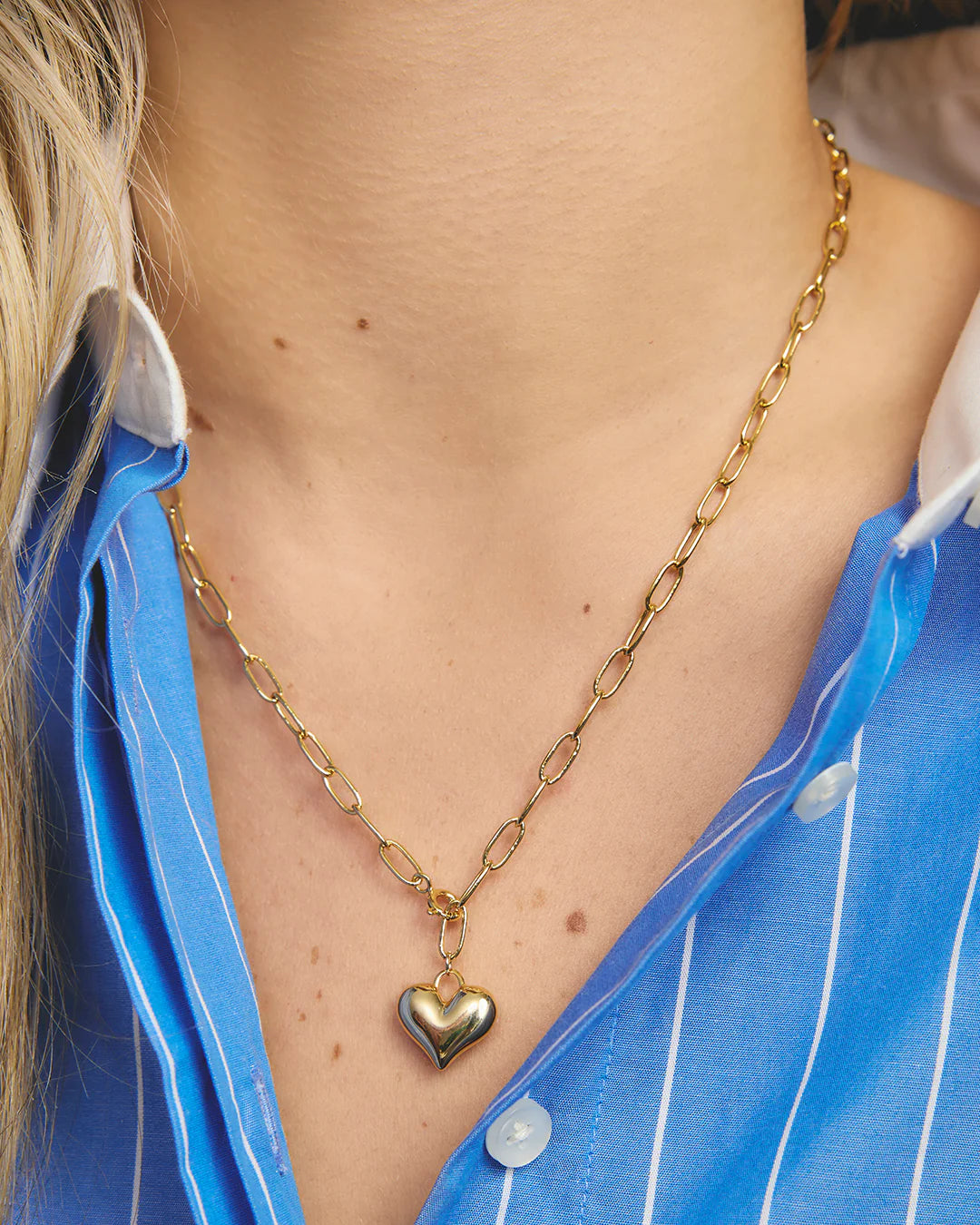 Gold chain necklace with a heart pendant worn by a person in a blue shirt.