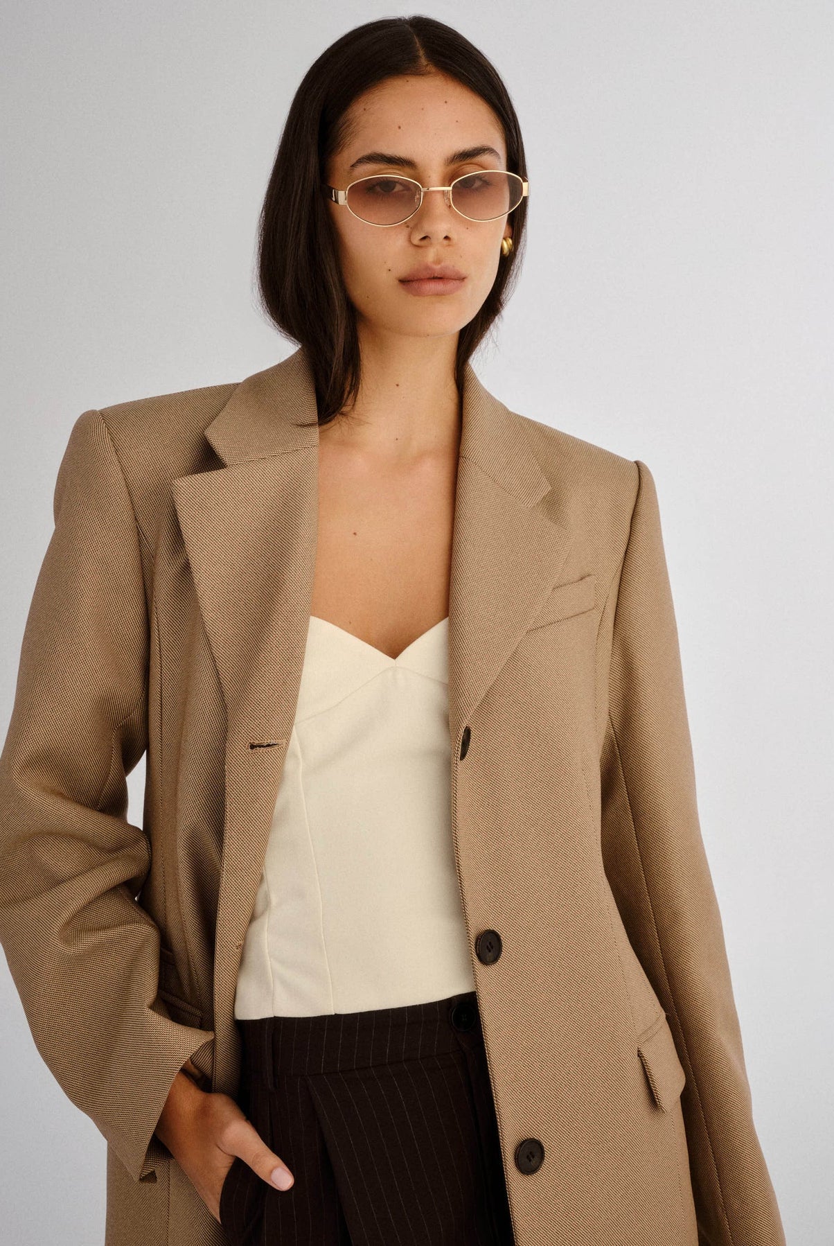 Woman wearing a beige blazer over a white top and black pants on a plain background