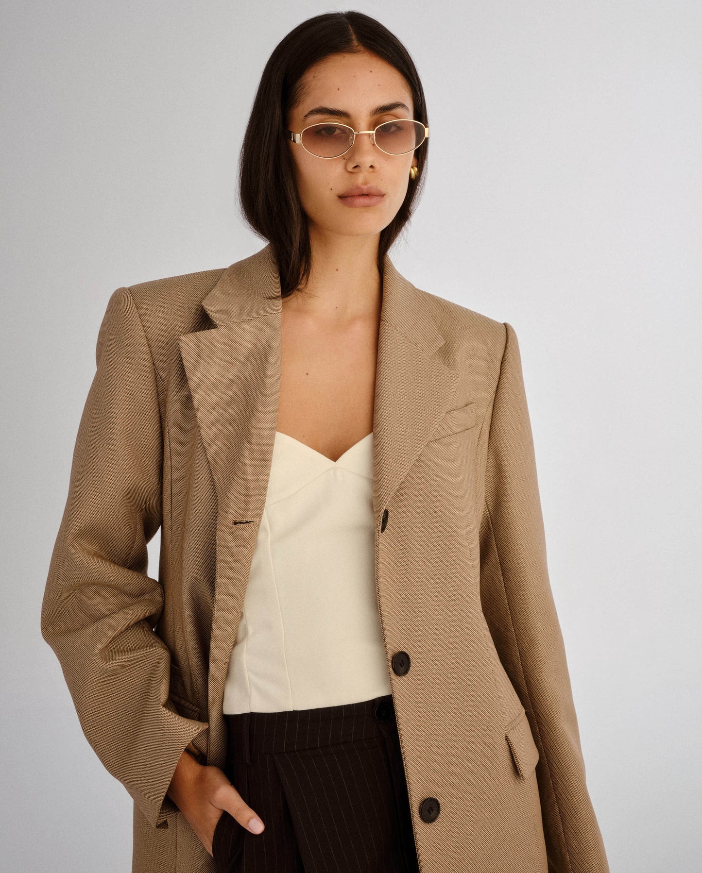 Woman wearing a beige blazer over a white top and black pants on a plain background