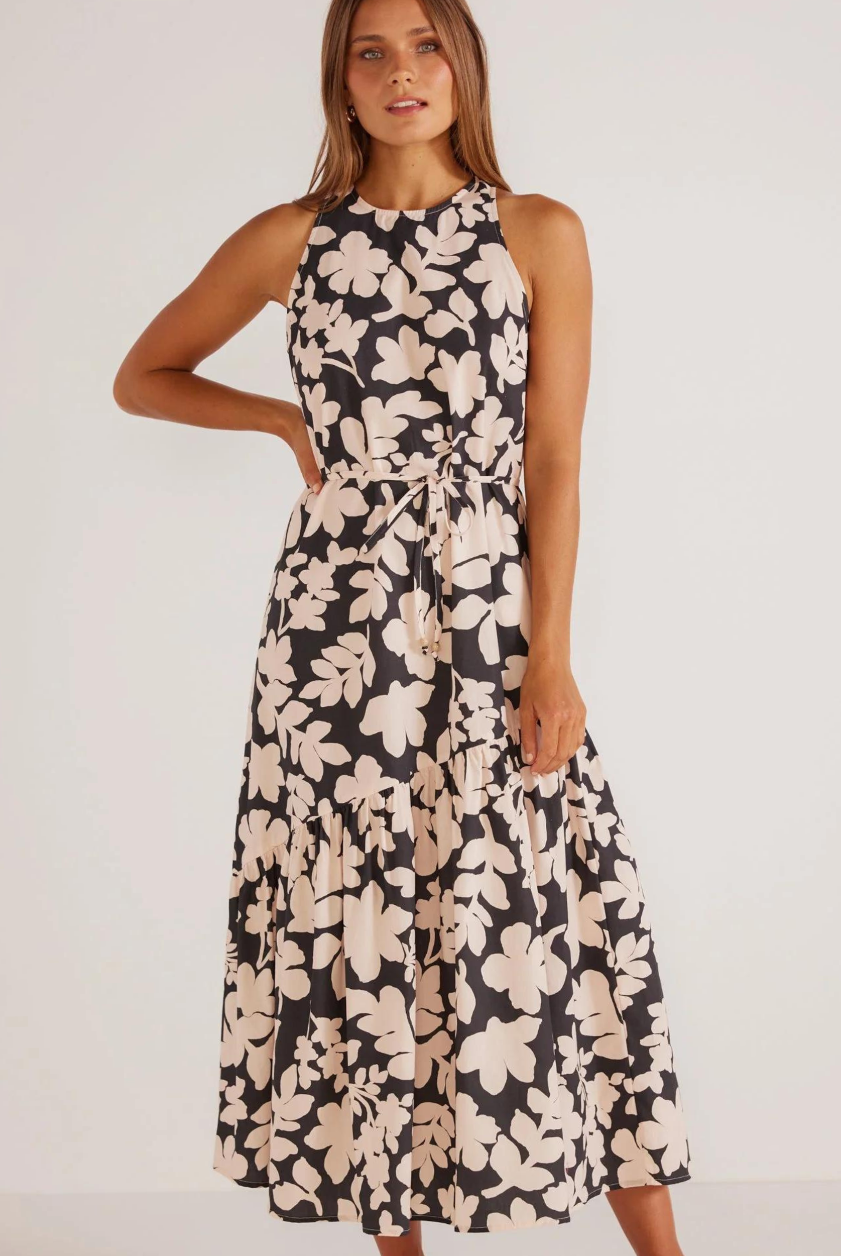 A sleeveless, midi-length dress with a floral print in beige and black, featuring a racer cut neckline, A-line silhouette, and side pockets.