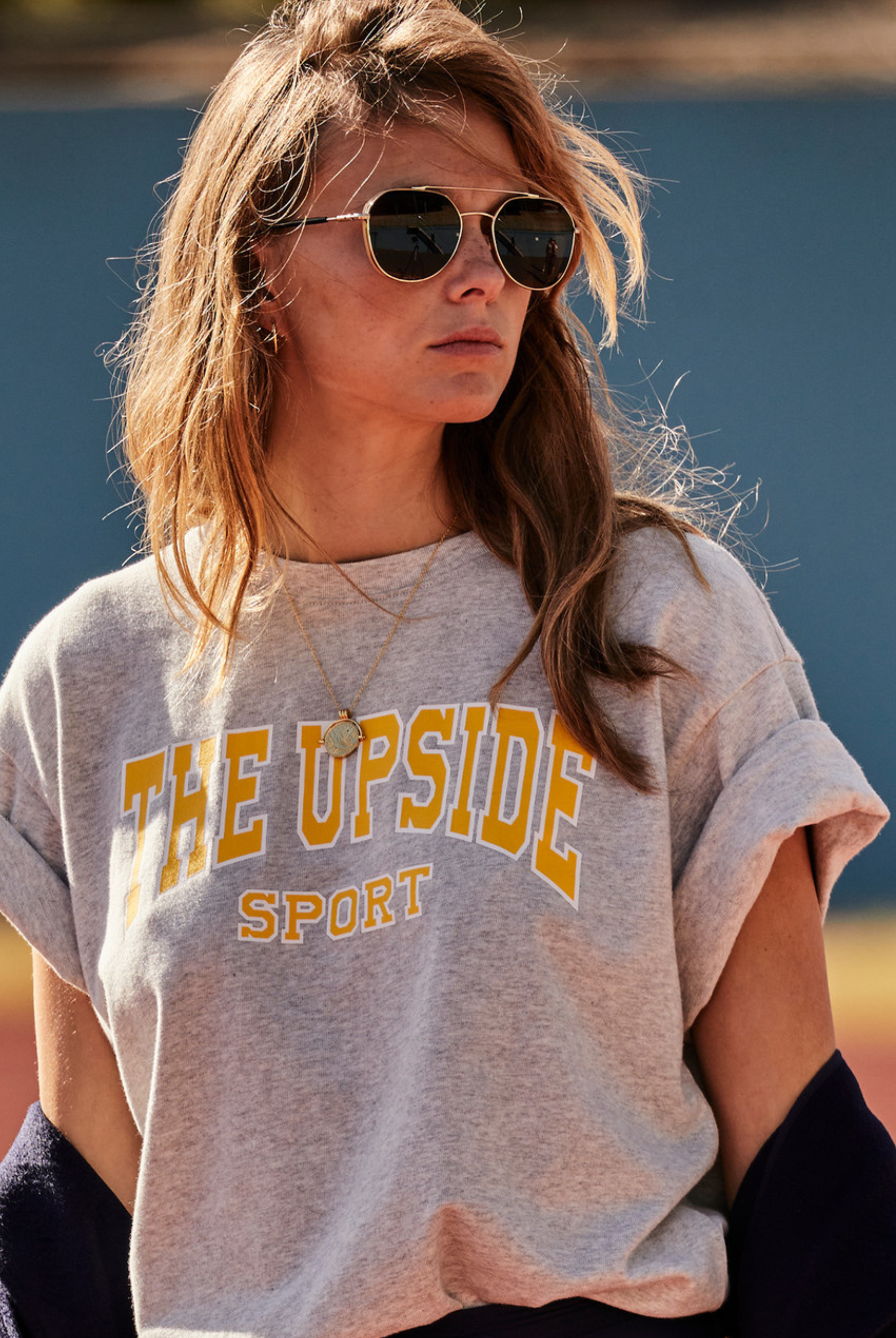 A woman wearing a light grey marle oversized t-shirt with 'THE UPSIDE sport' printed on the chest.