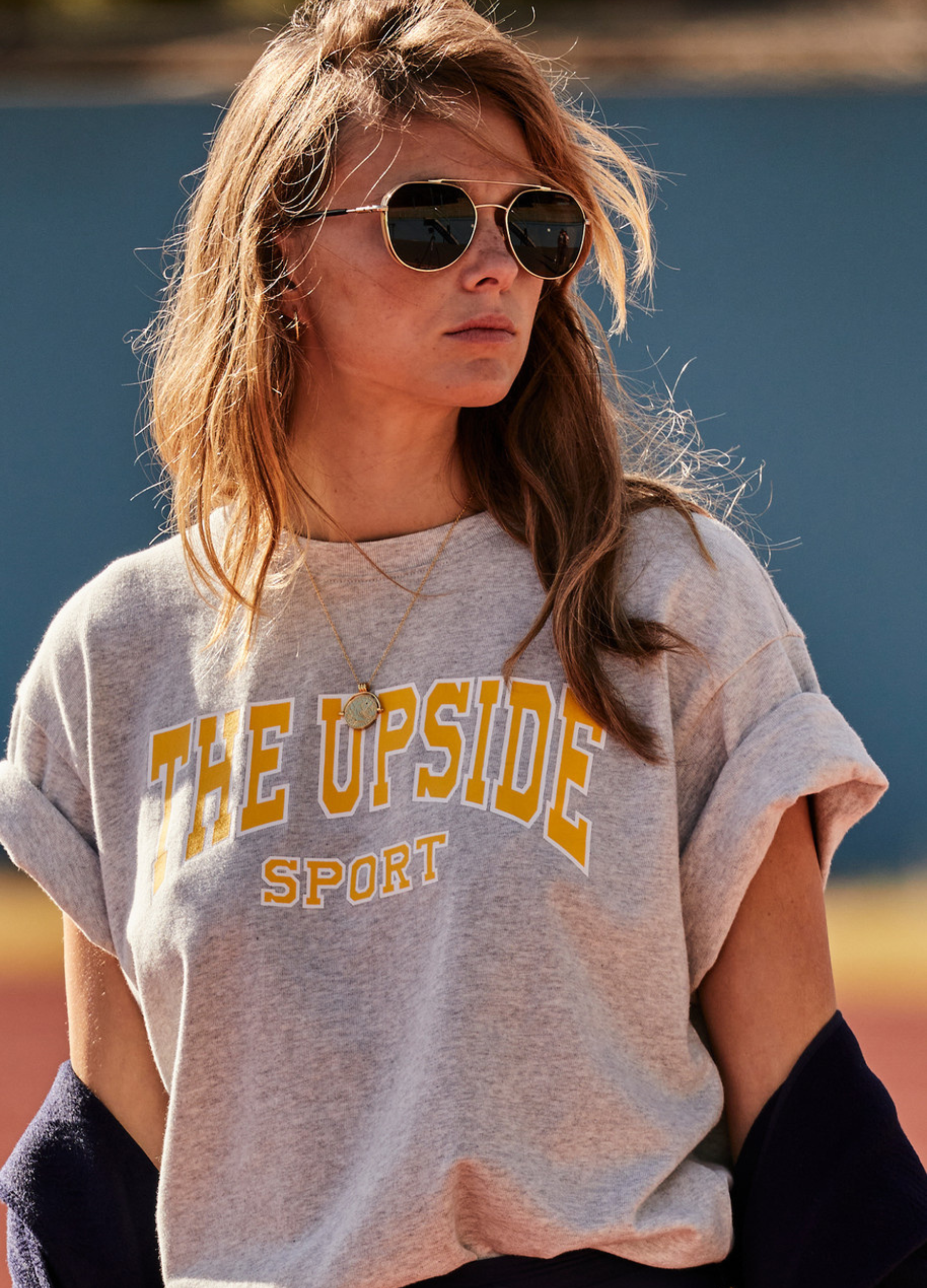 A woman wearing a light grey marle oversized t-shirt with 'THE UPSIDE sport' printed on the chest.