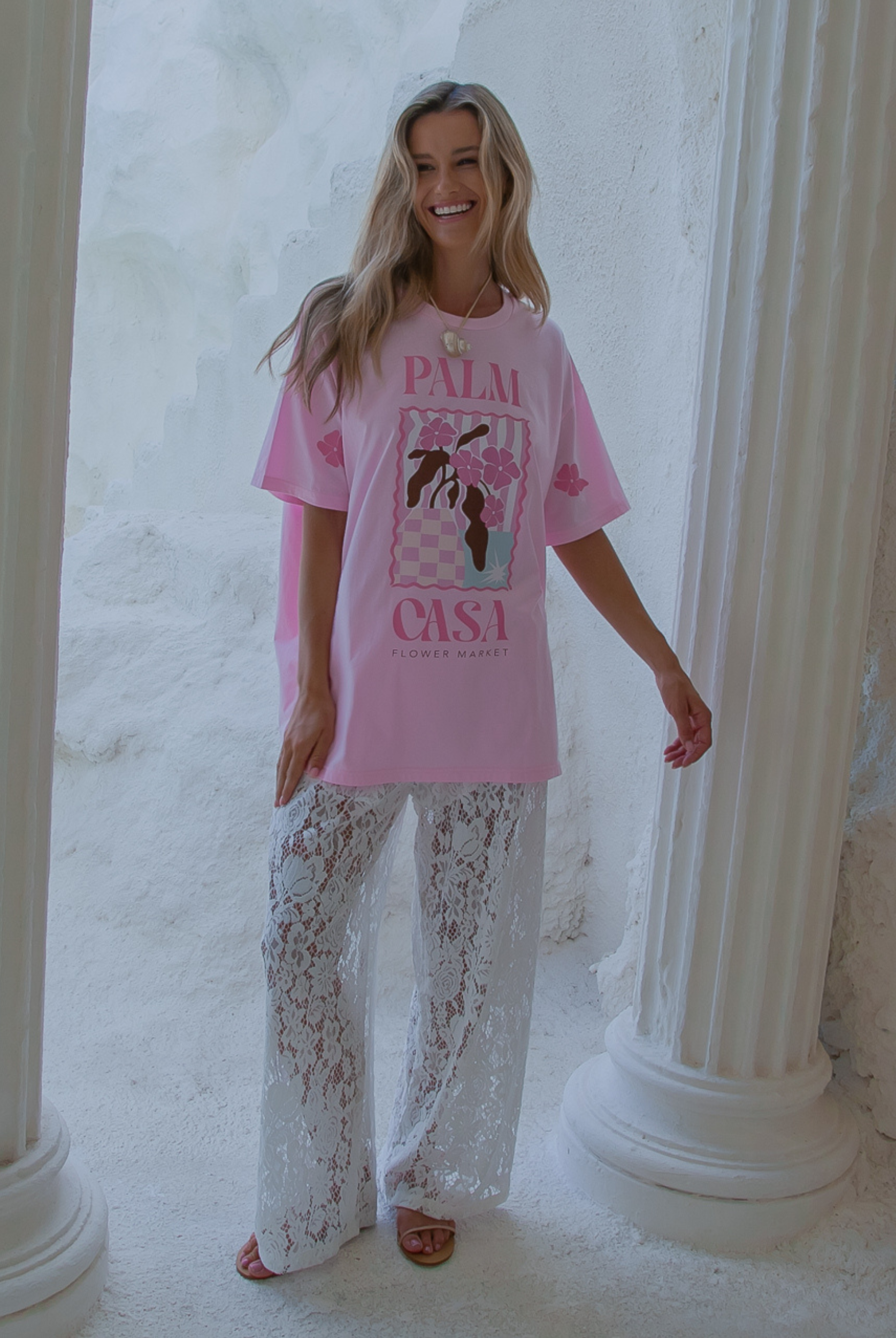Woman wearing a pink t-shirt with graphics and text, standing in a classical architecture setting.