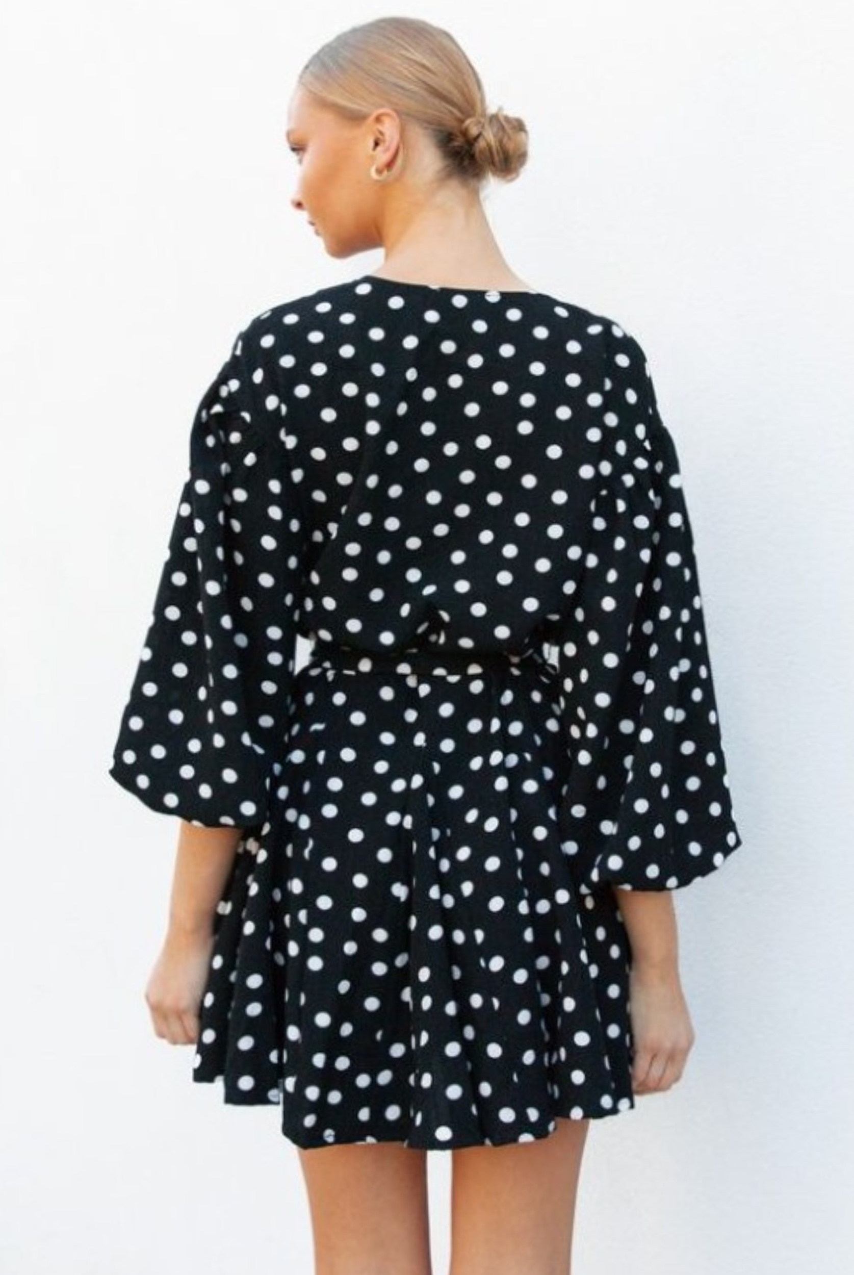 Model wearing black and white polka dot dress with waist belt and buttons