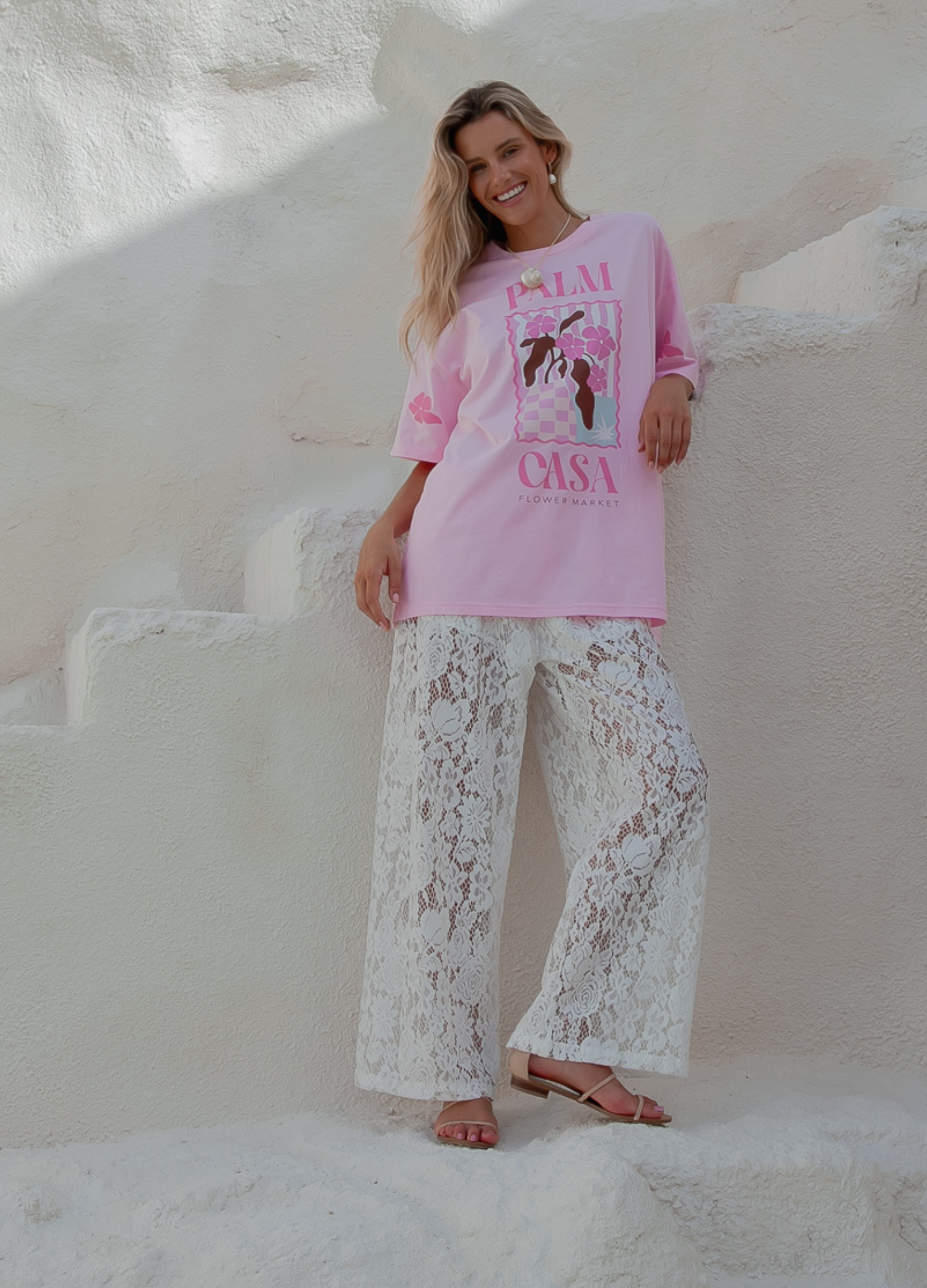 Woman wearing a pink sweatshirt with graphic design and white lace pants on a white background