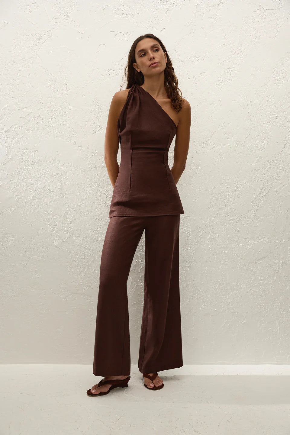 Woman wearing a brown halter top and wide-leg pants against a white background