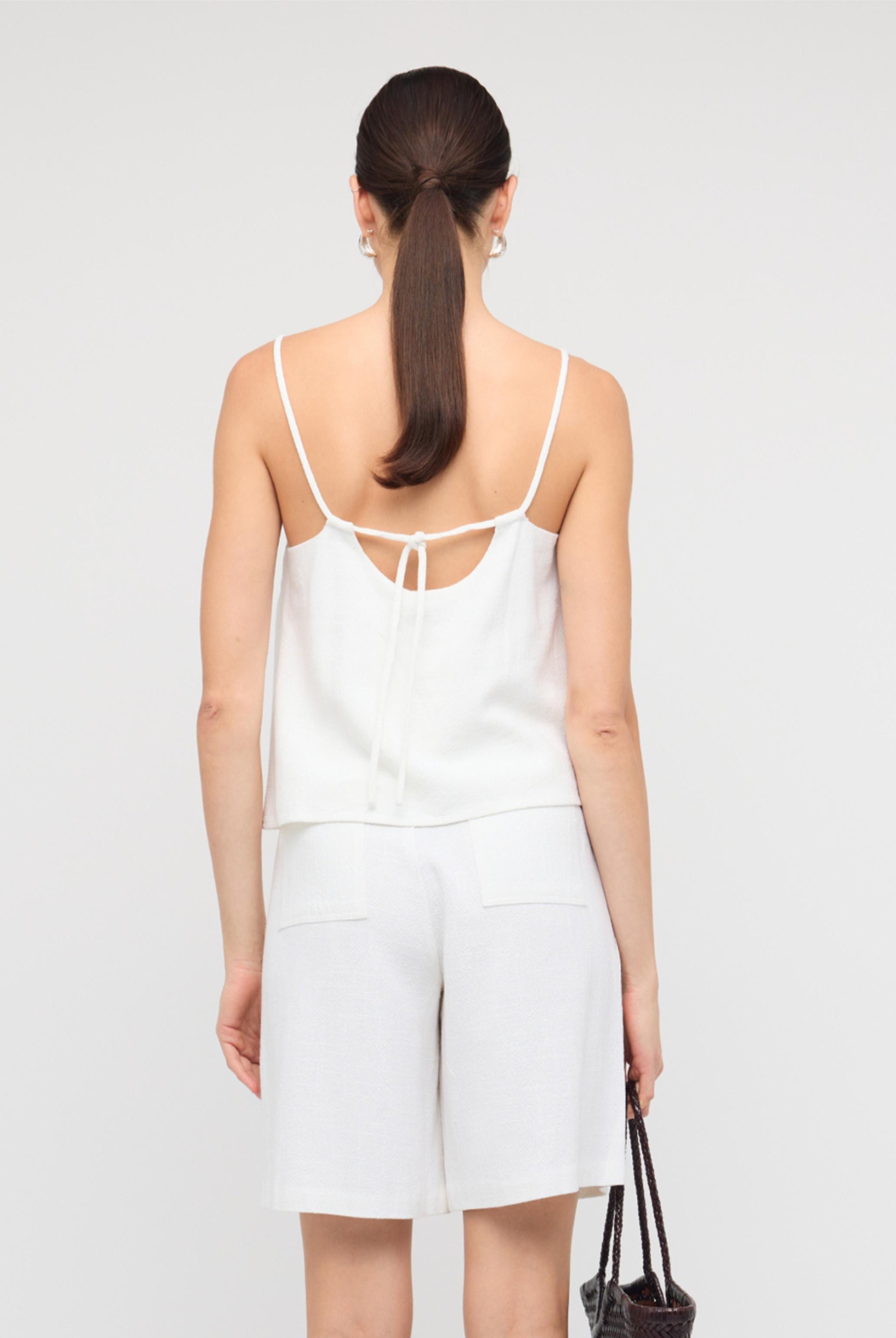 Woman wearing a white dress with thin straps on a plain background