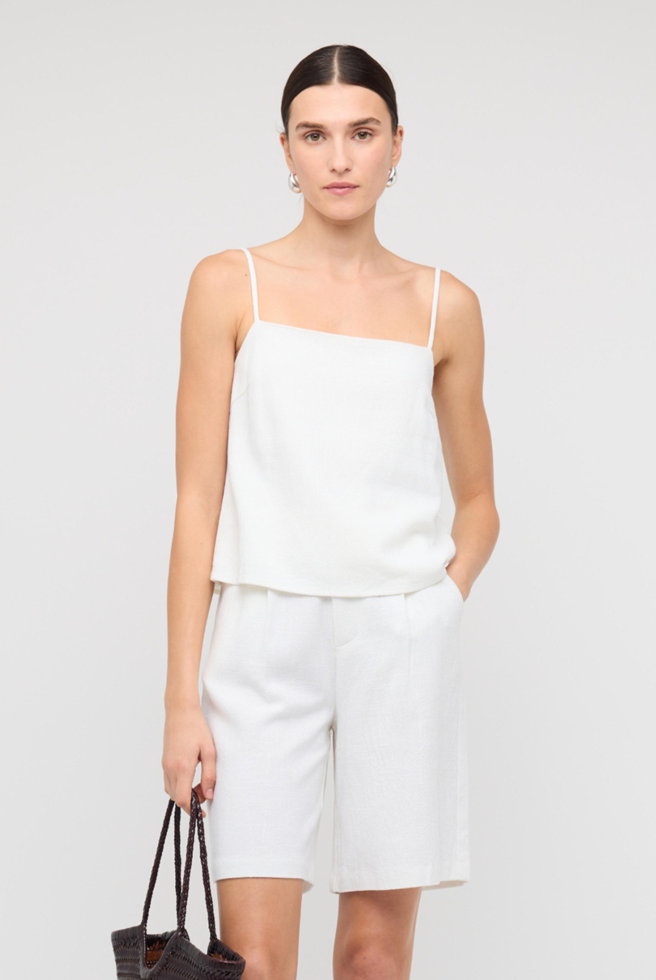 Woman wearing a white sleeveless top and shorts on a plain background