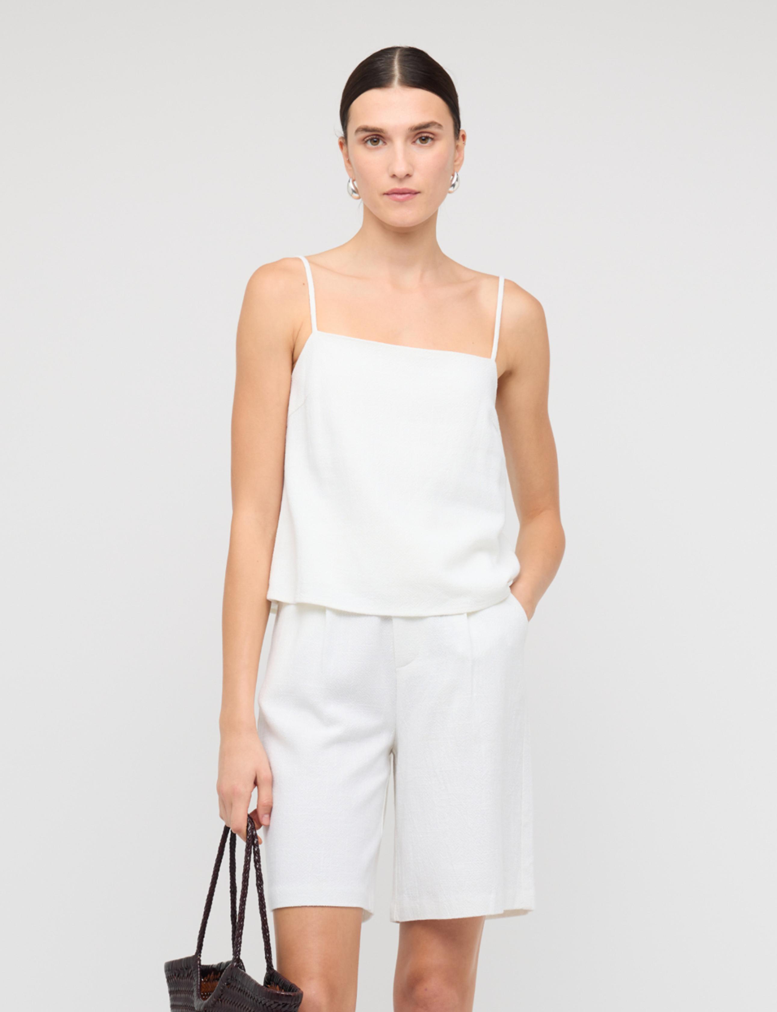 Woman wearing a white sleeveless top and shorts on a plain background