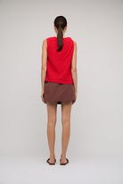 Woman wearing a red sleeveless top and brown skirt on a plain background