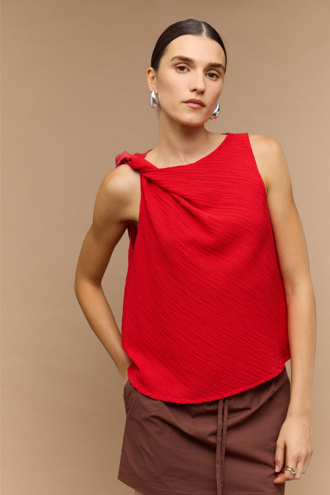 Woman wearing a red sleeveless top with a knot detail on a beige background