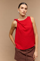 Woman wearing a red sleeveless top with a knot detail on a beige background
