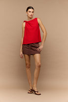 Woman wearing a red sleeveless top and brown shorts against a beige background