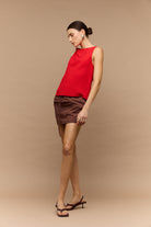 Woman wearing a red sleeveless top and brown shorts on a beige background