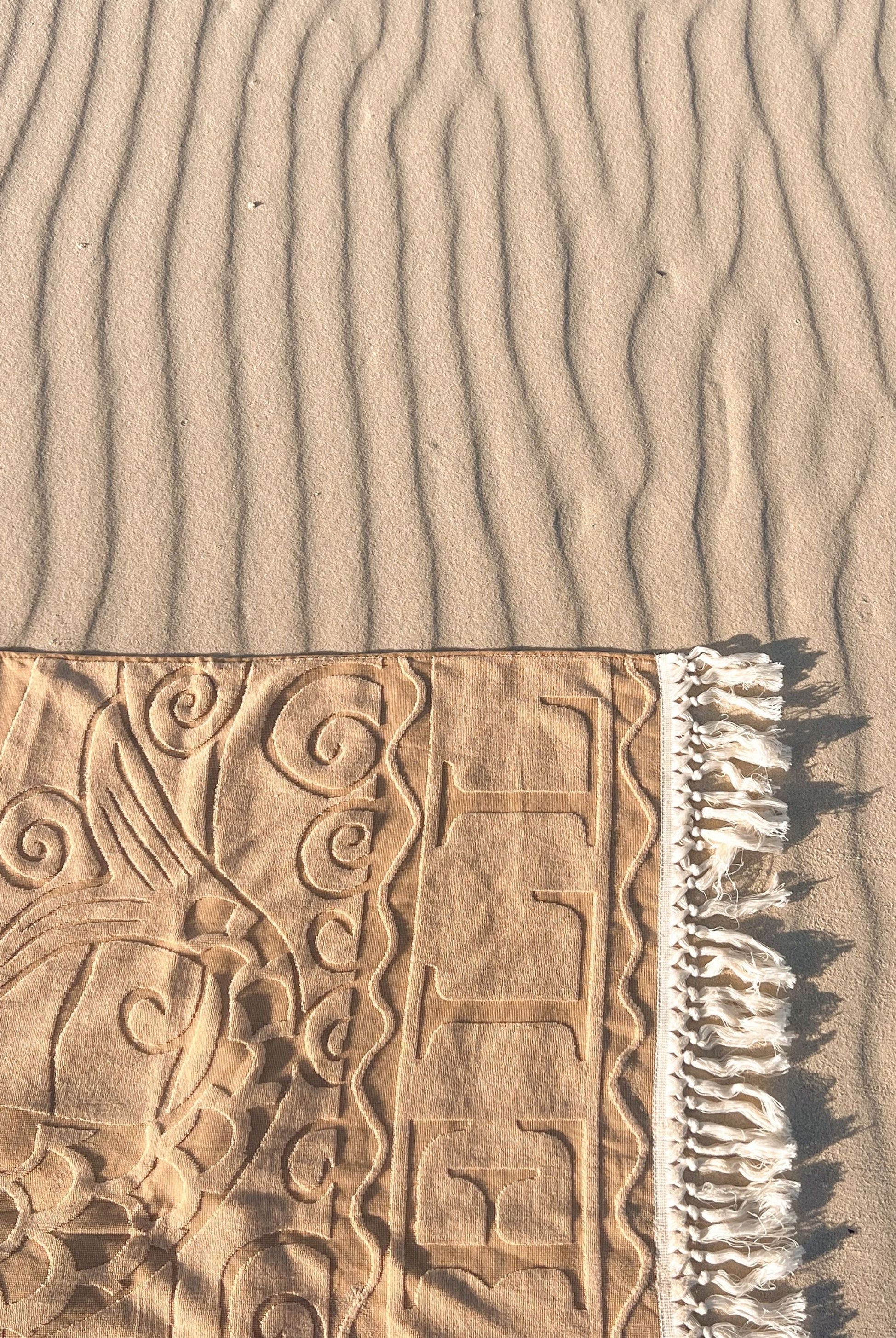 Textured sand surface with a beach towel featuring intricate patterns and fringes.