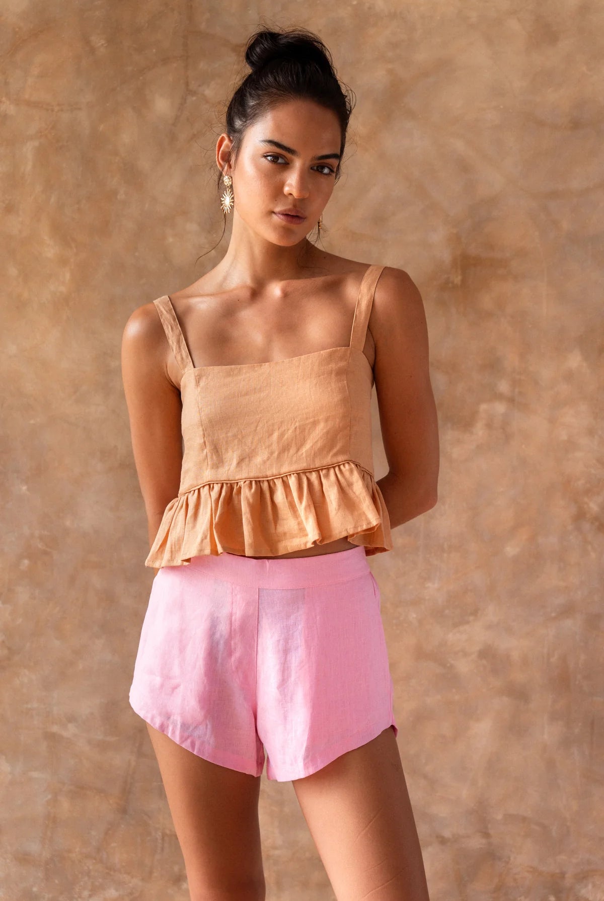 Woman wearing a peach top and pink shorts against a beige background