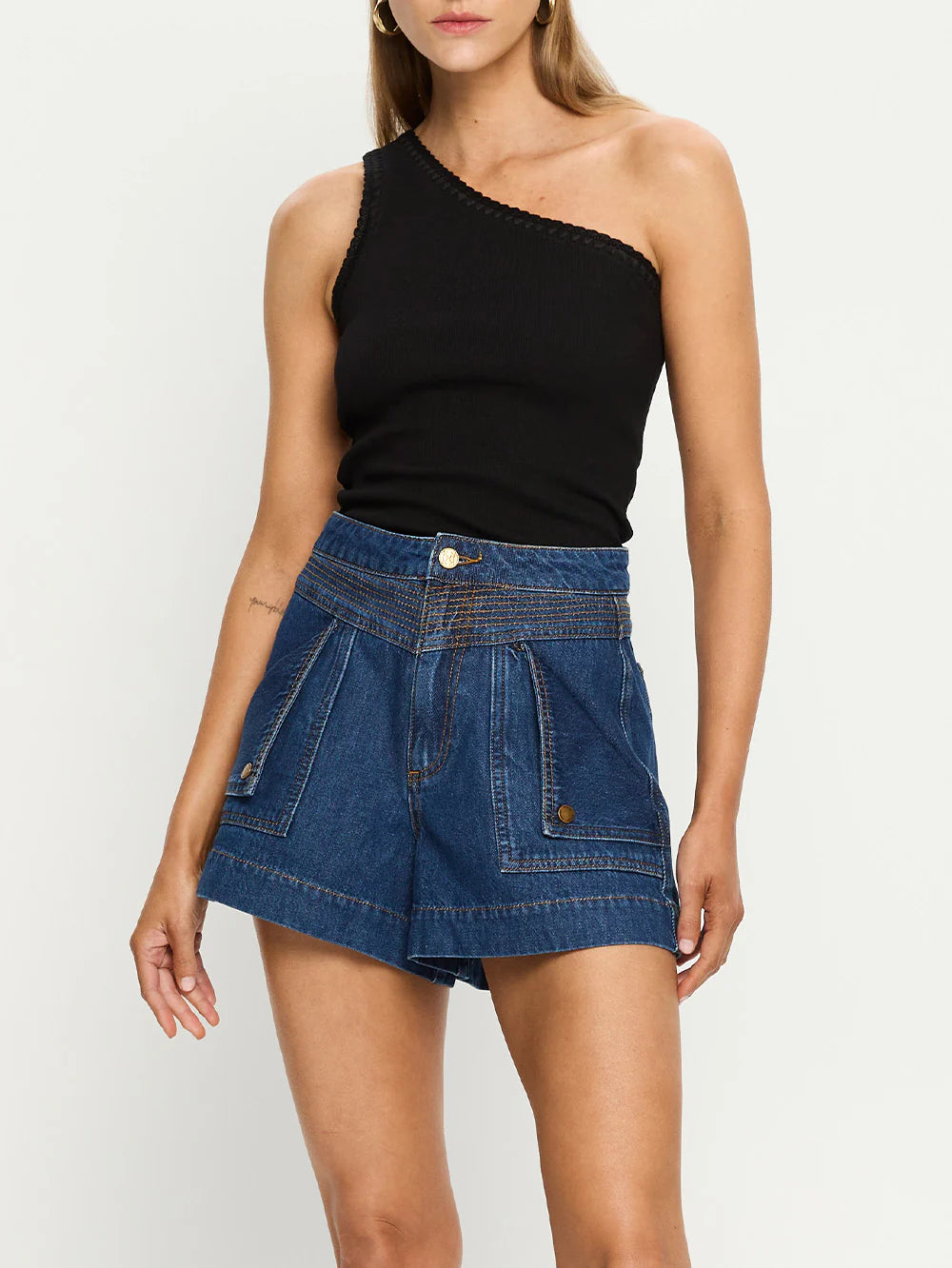 Woman wearing a black one-shoulder top and blue denim shorts on a white background