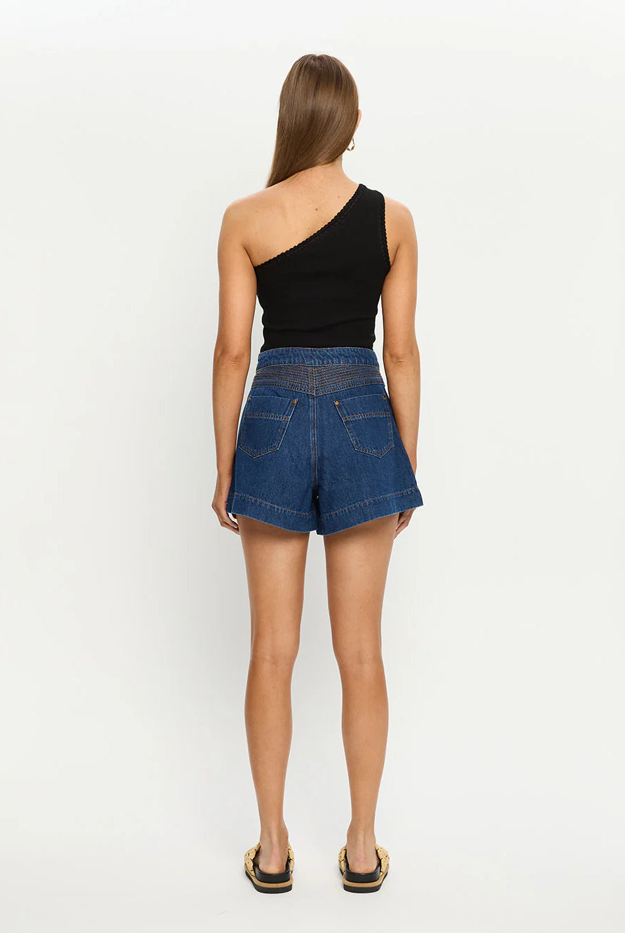 Woman wearing blue denim shorts and a black one-shoulder top on a white background