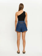 Woman wearing blue denim shorts and a black one-shoulder top on a white background
