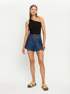 Woman wearing a black one-shoulder top and blue denim shorts on a white background