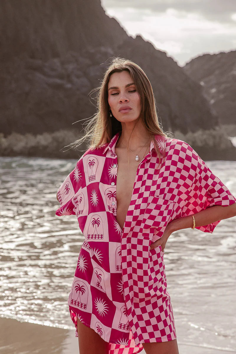 Woman wearing a pink and white patterned cover-up by a body of water with mountains in the background