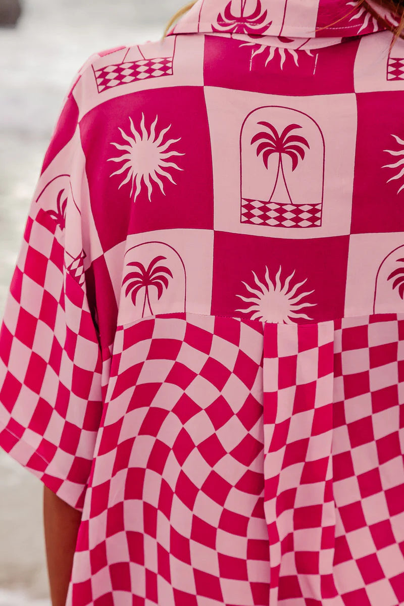 Close-up of a pink and red patterned garment with palm tree and sun designs.