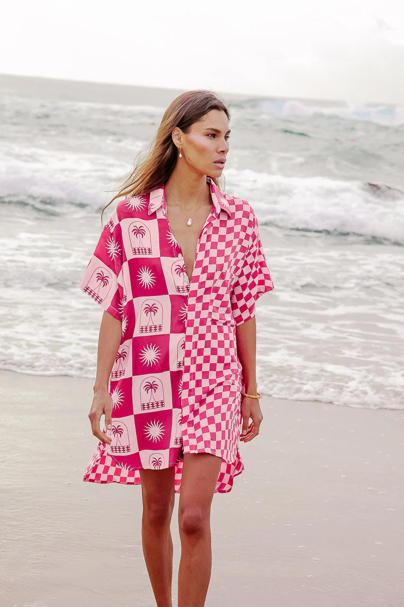 Woman wearing a pink and white patterned dress on a beach.