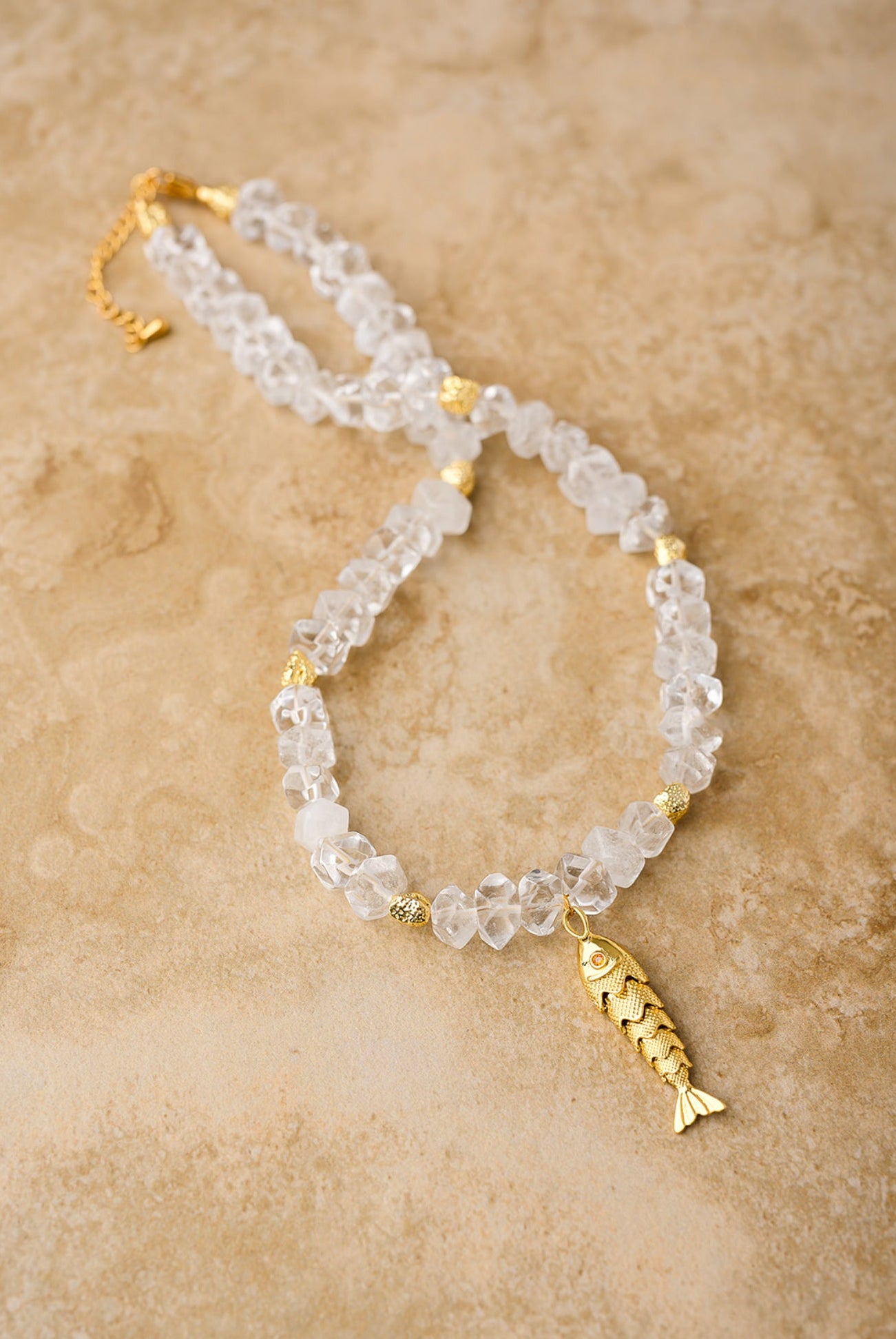 Necklace with clear beads and gold fish charm on a beige background