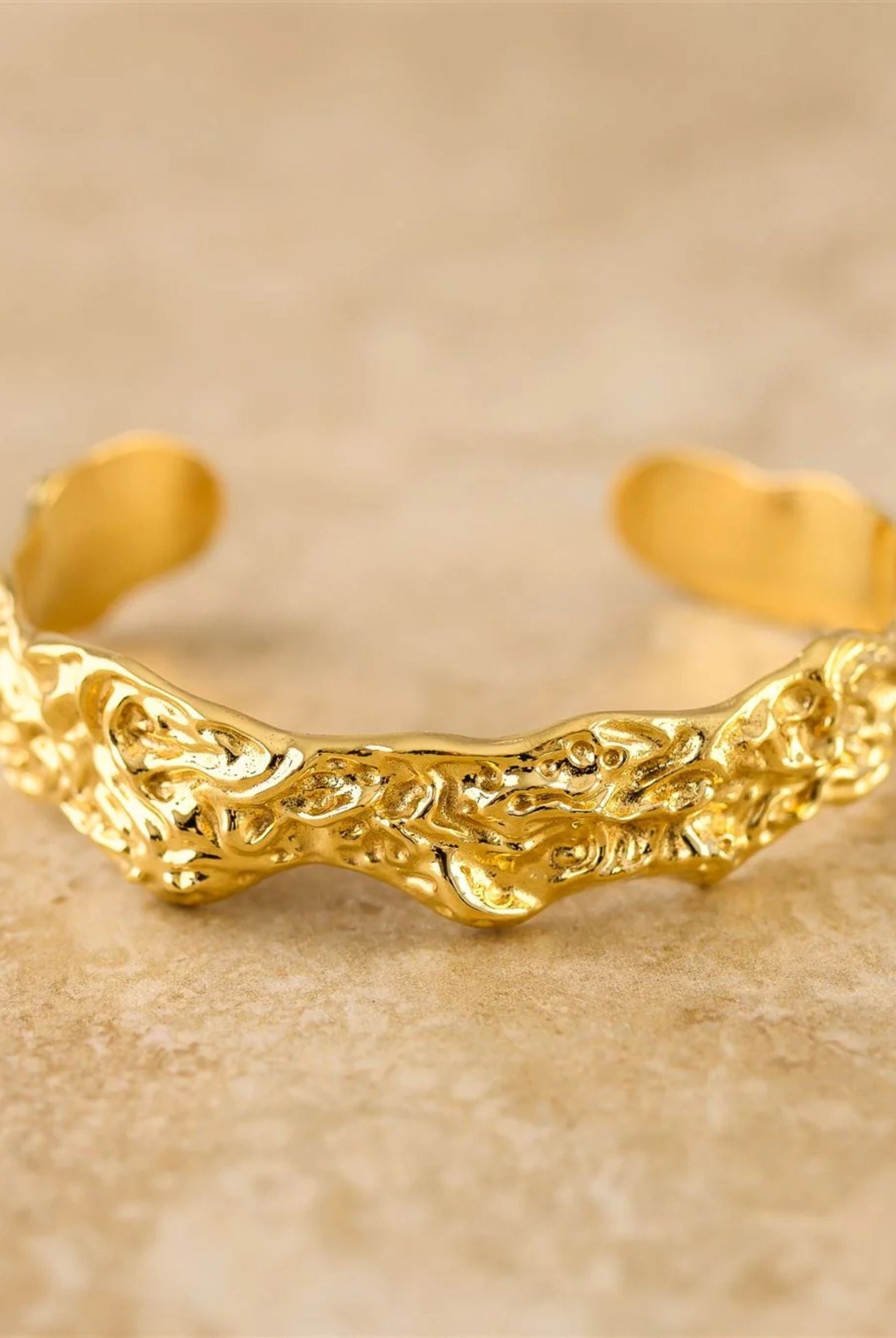 Gold bracelet with intricate design on a beige background
