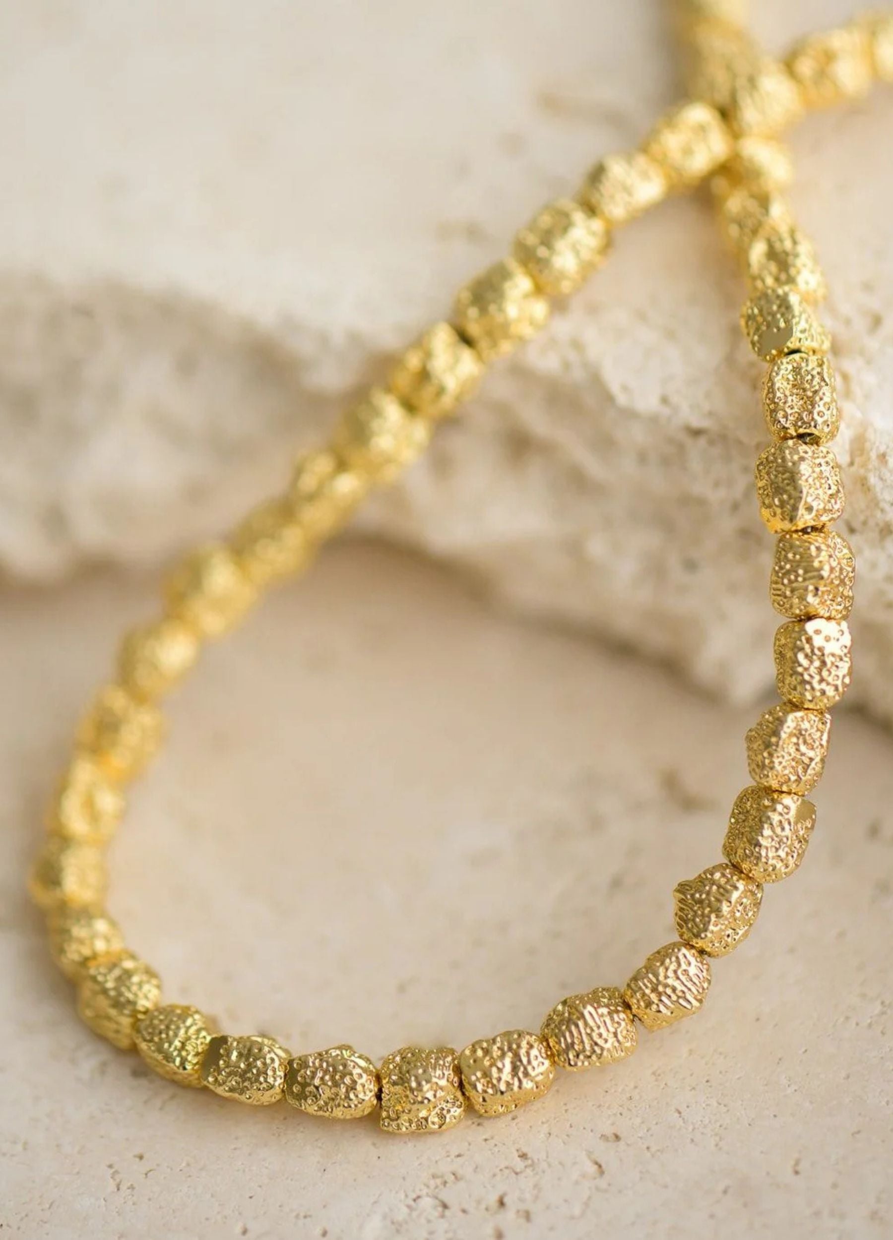 Gold beaded necklace on a textured beige surface