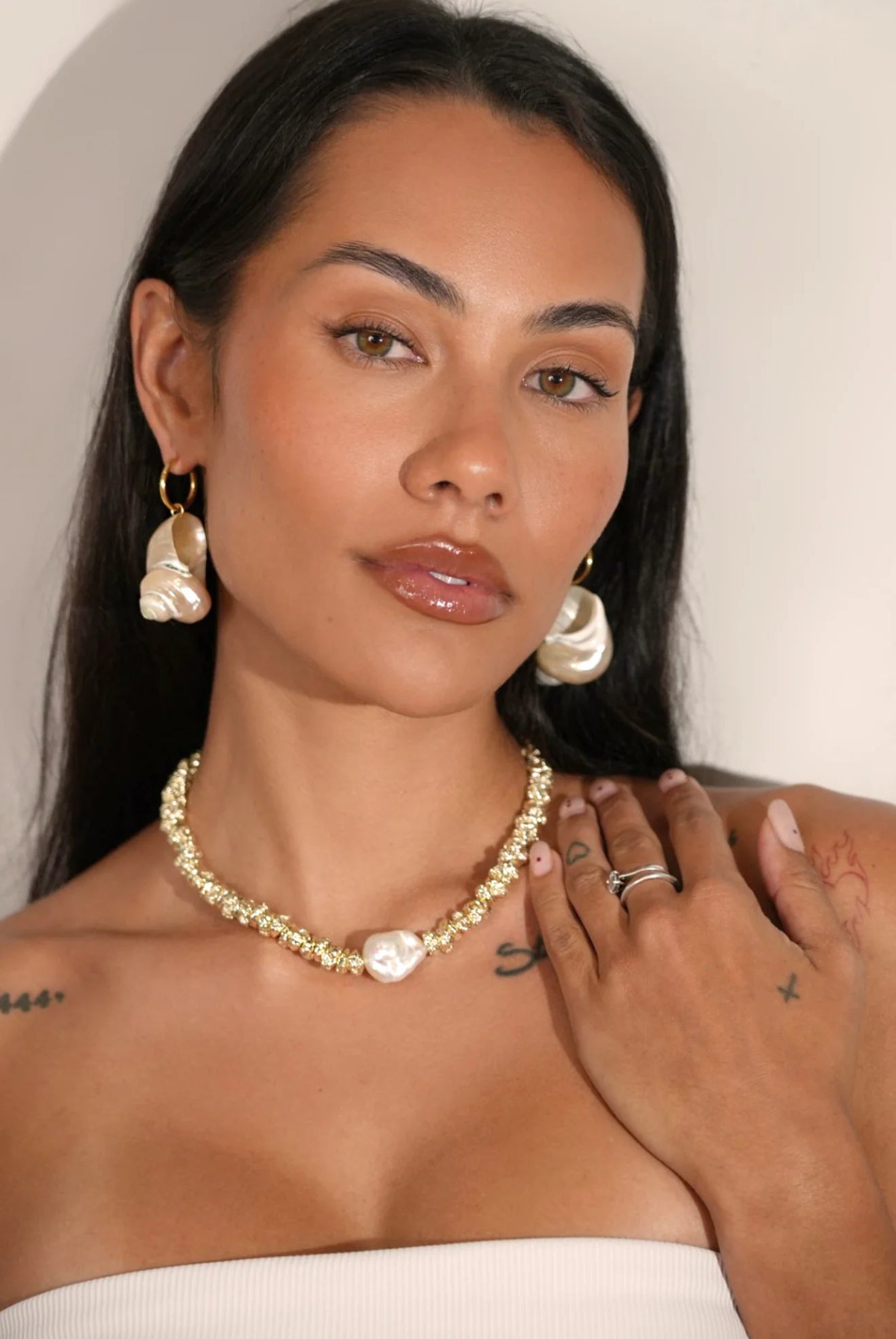 Woman wearing a gold necklace and pearl earrings with a neutral background