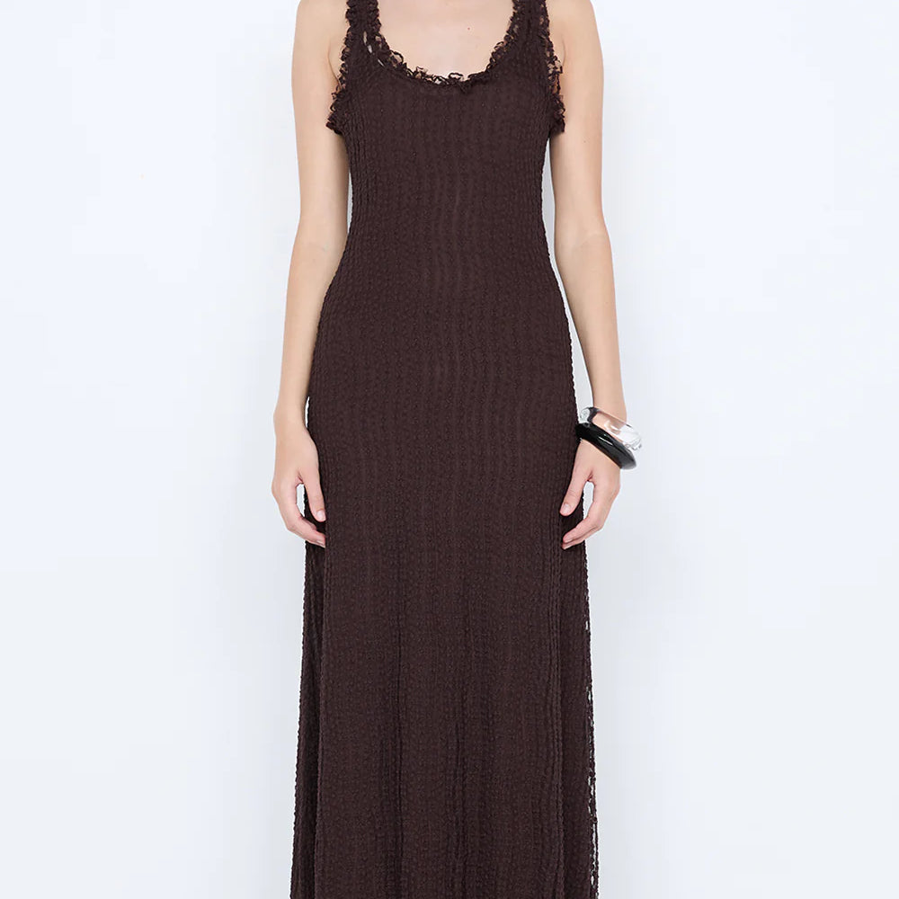 Woman wearing a long brown dress with lace details on a white background