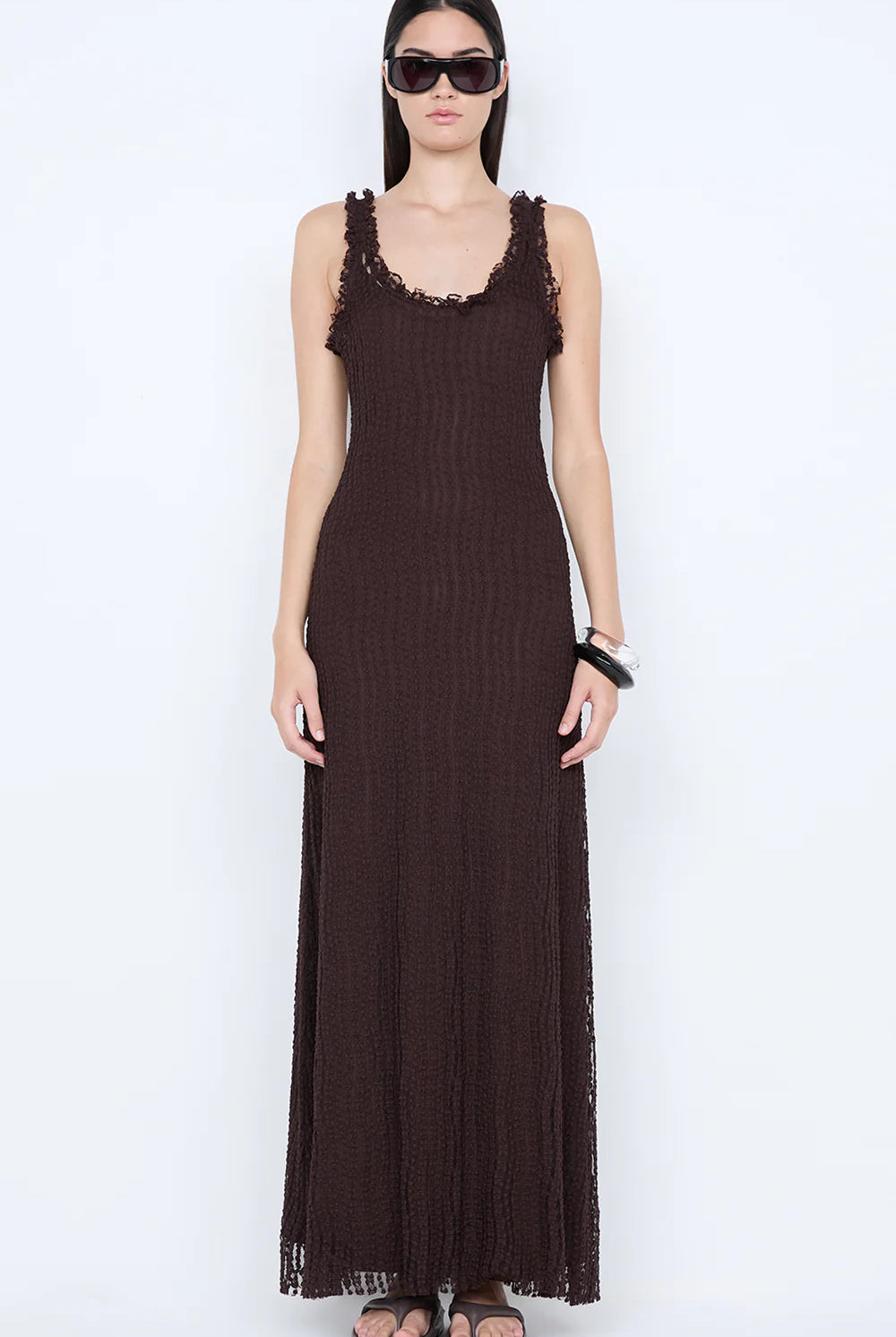 Woman wearing a long brown dress with lace details on a white background