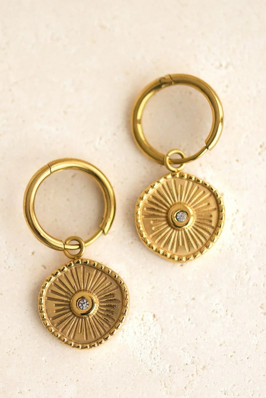 Pair of gold hoop earrings with circular designs on a beige background