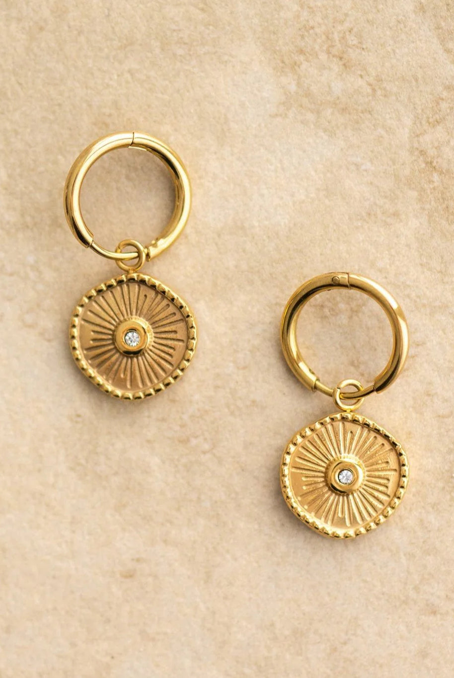 Pair of gold hoop earrings with circular designs on a beige background