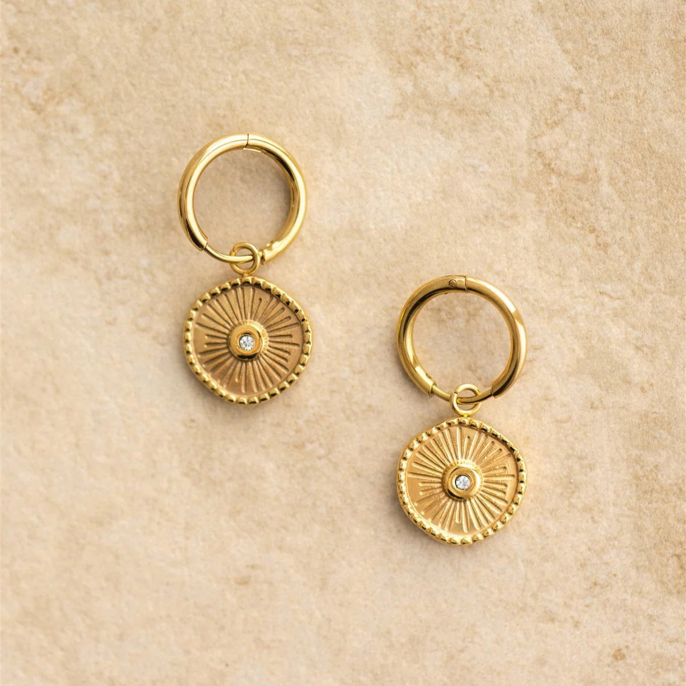 Pair of gold hoop earrings with circular designs on a beige background