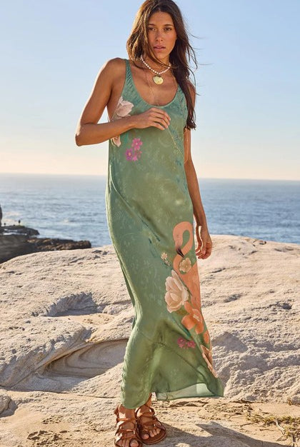 Woman in a green floral dress standing on a beach with ocean in the background