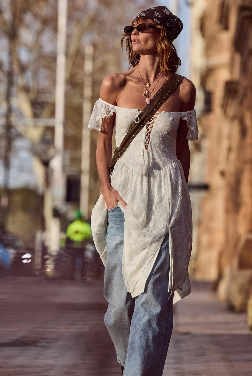 Woman in a white off-shoulder dress and blue jeans walking outdoors.