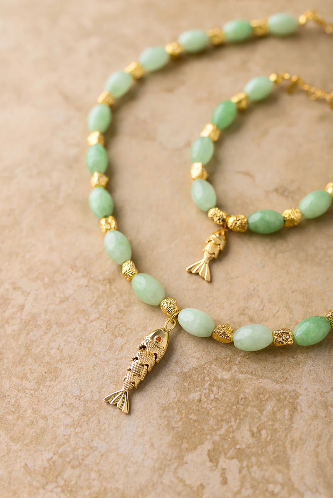 Necklace with gold fish pendants and green beads on a beige background