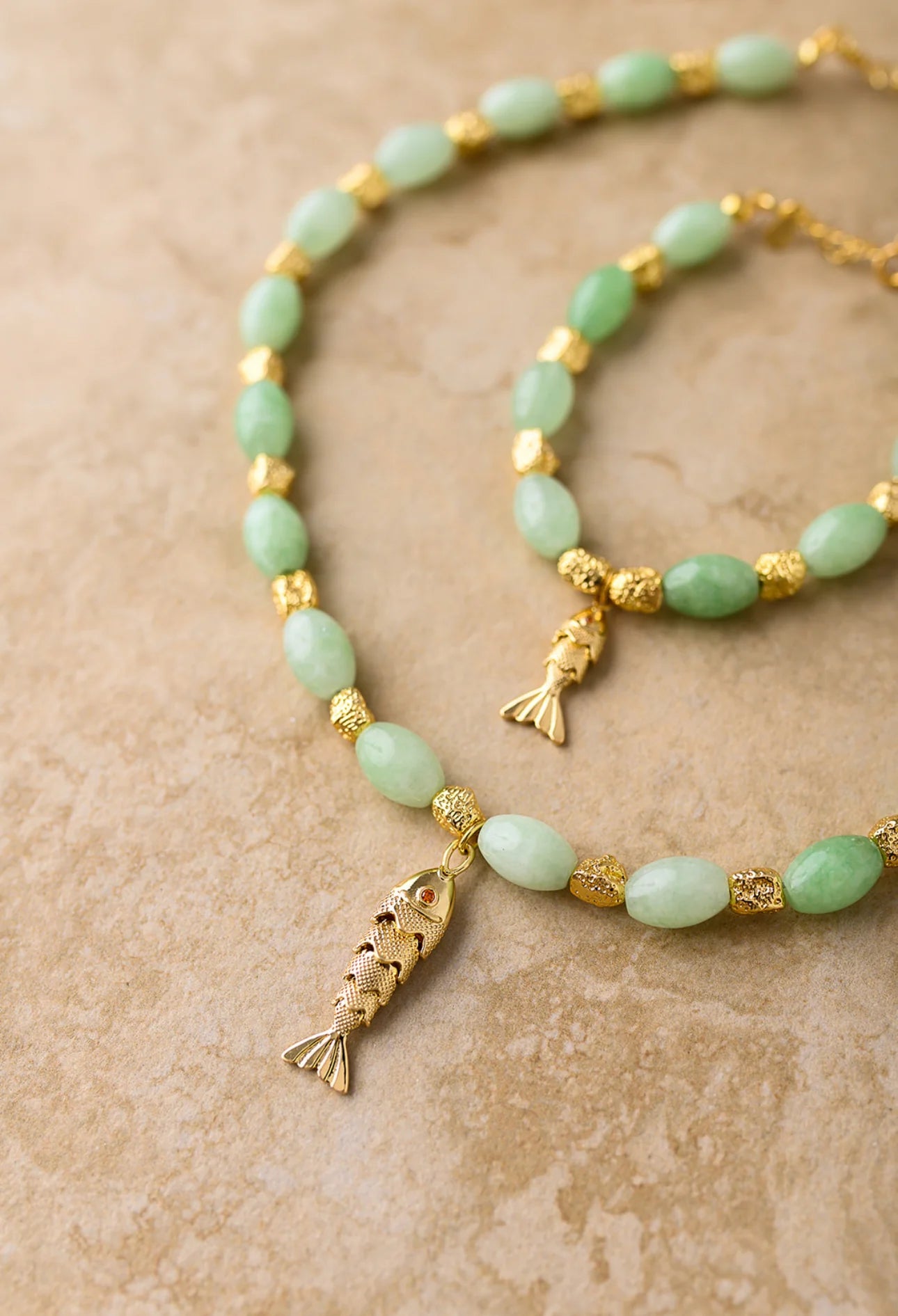 Necklace with gold fish pendants and green beads on a beige background