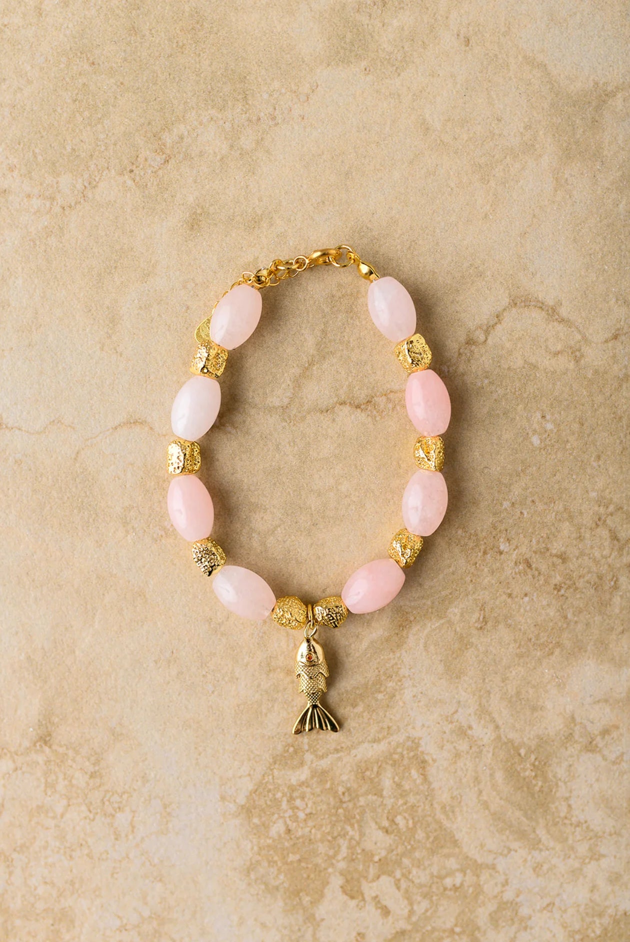 Bracelet with pink beads and gold accents on a beige marble background