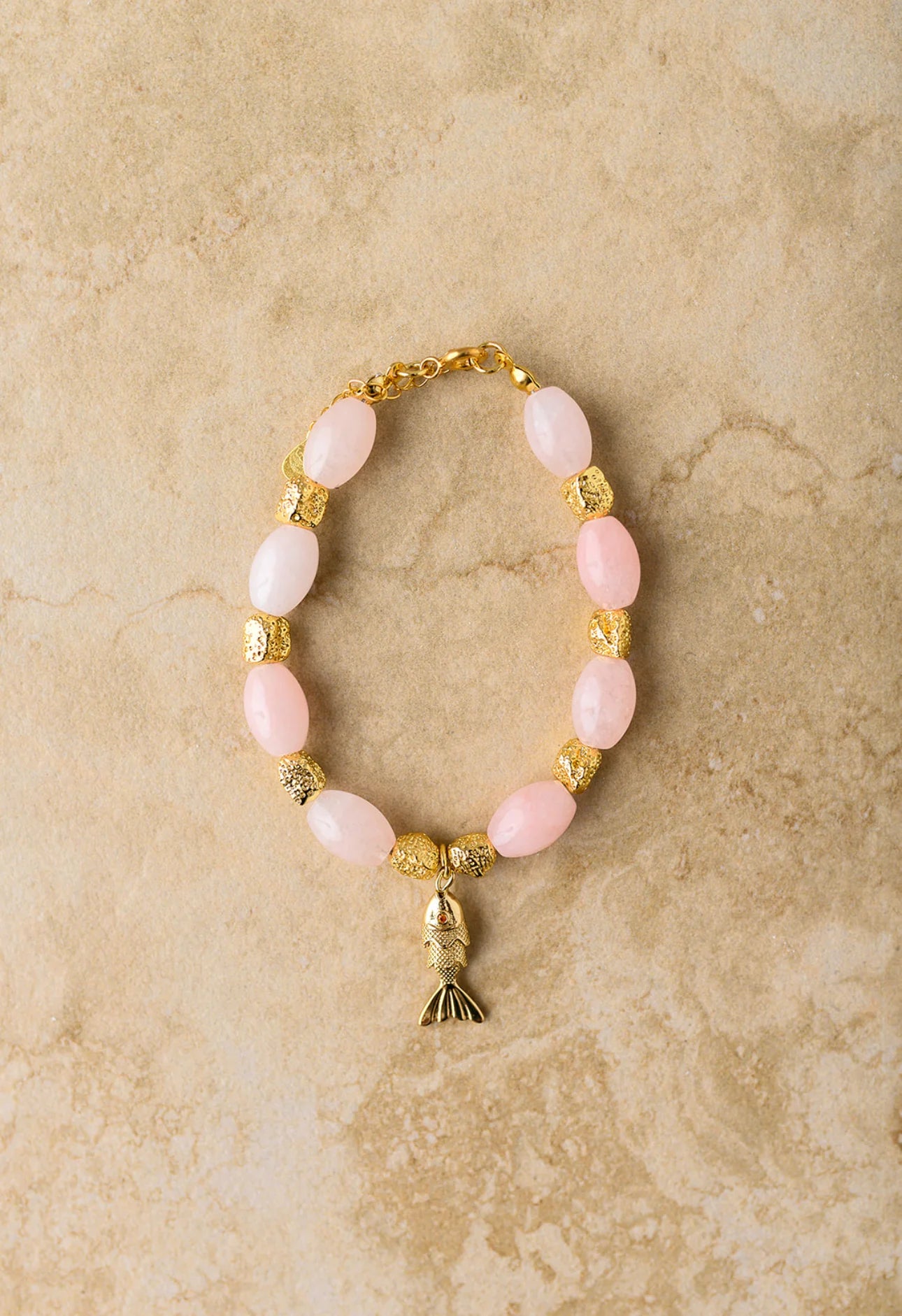 Bracelet with pink beads and gold accents on a beige marble background
