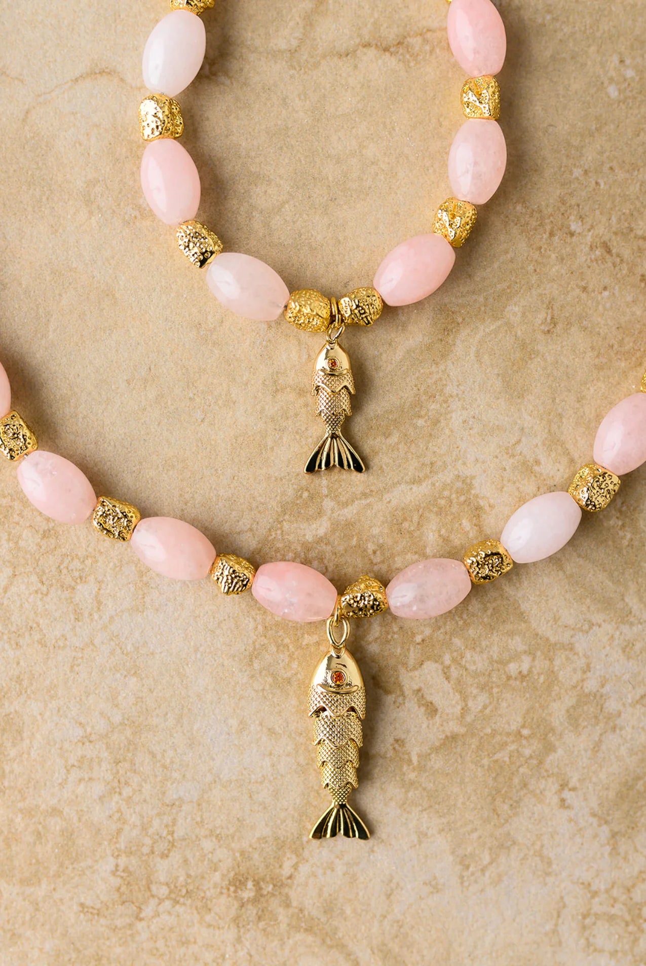 Necklace with pink beads and gold fish pendants on a beige background