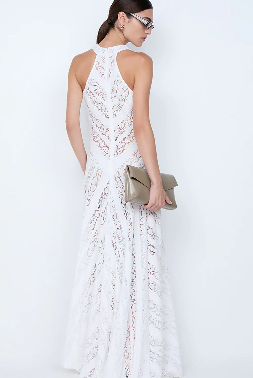 Woman wearing a white lace dress holding a beige clutch against a white background