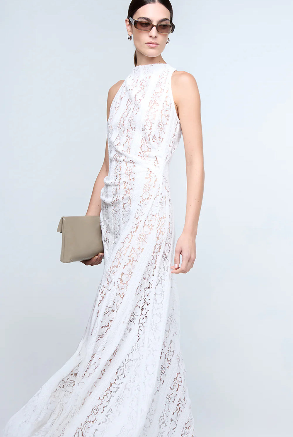 Woman wearing a white lace dress holding a clutch against a light gray background